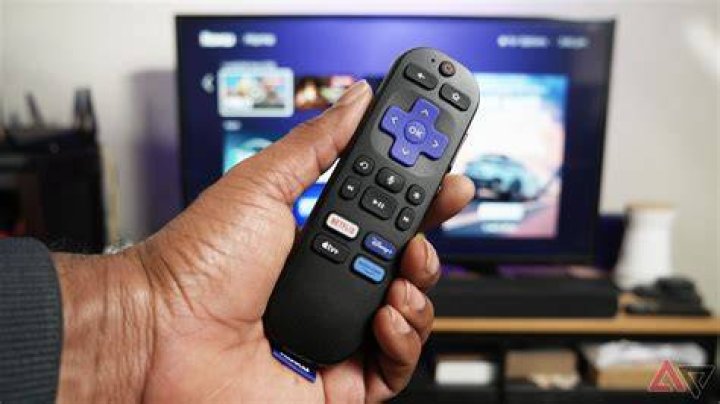 Roku remote in front of a TV running Roku OS